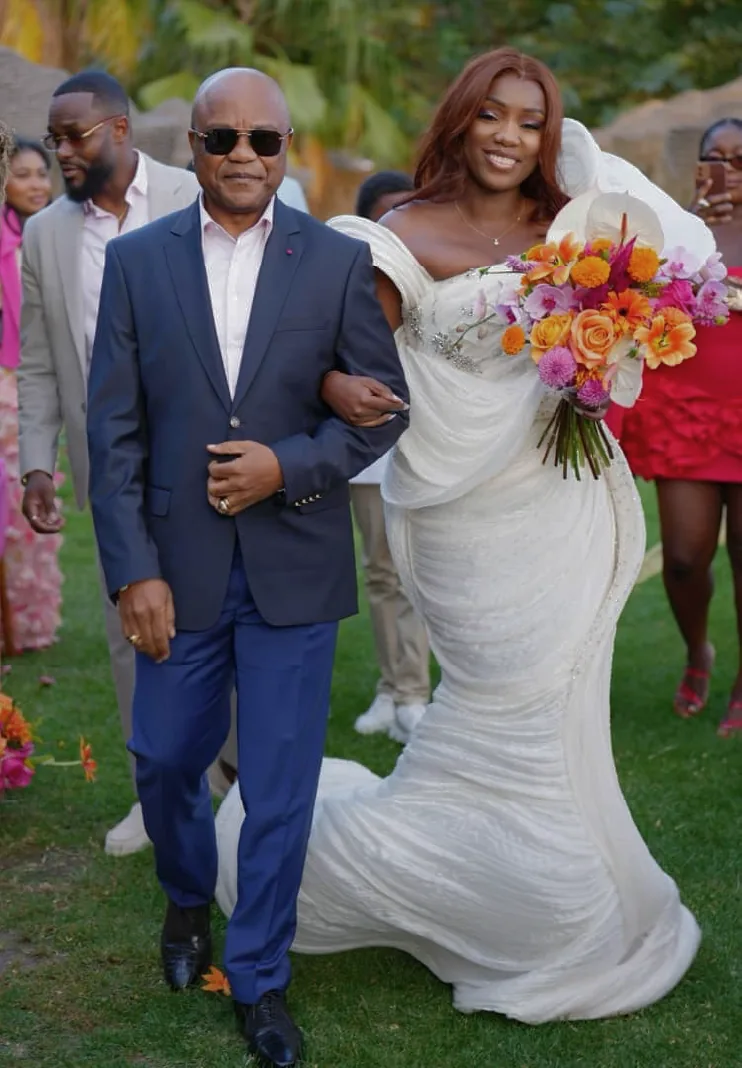 A bride in a white off-shoulder gown beside orange blossoms
